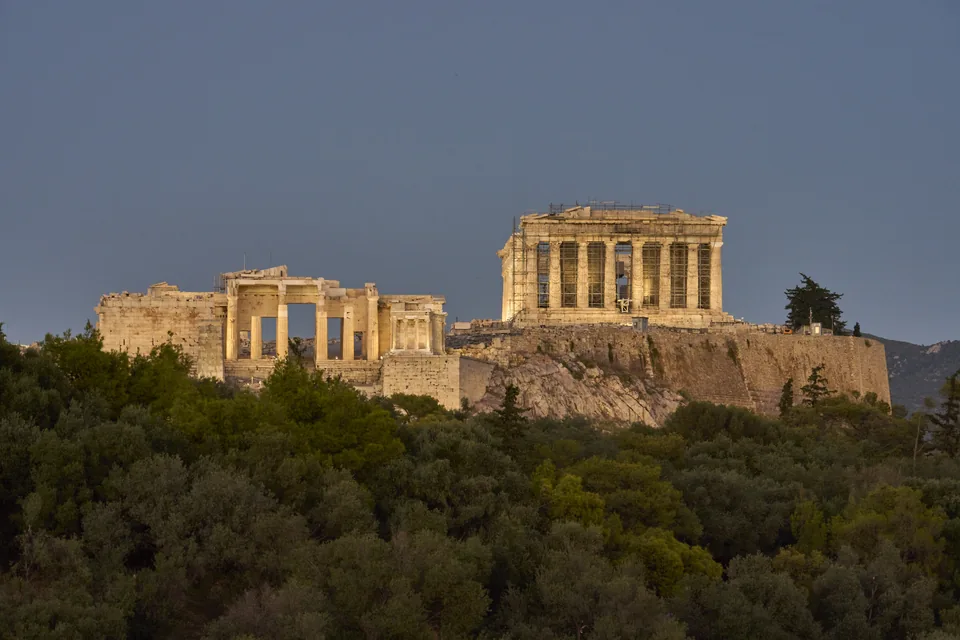 The Acropolis of Athens lit at dusk above the trees of Melite